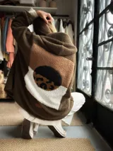 Campera estilo sherpa color verde militar, con capucha y diseño oversize. Presenta un gran aplique geométrico en la espalda en tonos tostado, blanco y un círculo con estampado animal print.