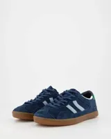 Championes de estilo urbano confeccionados en gamuza azul marino, con detalles en celeste claro en los laterales y refuerzo verde en el talón. Presentan suela de goma color caramelo y cierre mediante cordones al tono.
