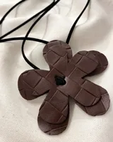 Gargantilla con dije de flor de cuero marrón con diseño trenzado y cordón negro.