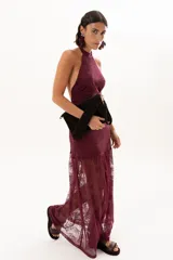 Vestido largo de encaje color bordó, con escote halter y diseño ajustado en el torso que se extiende hasta la cintura, donde continúa con una falda larga de encaje transparente.