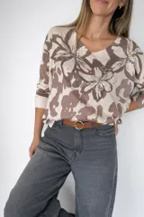 Sweater de tejido fino y liviano con cuello en V y mangas largas. Presenta un estampado floral tipo print en tonos beige y marrón, decorado con aplicaciones de strass que forman motivos de tréboles y la palabra LOVE.