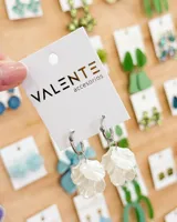 Aros de tipo argolla pequeña de acero con dije colgante en forma de pétalos de flor en color blanco perlado.