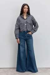 Camisa de corte cropped y estilo oversize, con estampado de rayas verticales en tonos azul, blanco y naranja. Presenta cuello clásico, cierre frontal con botones y dos bolsillos tipo cargo en el pecho.