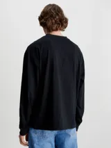 Remera de manga larga Calvin Klein Jeans, color negro, con corte oversized y cuello redondo. Presenta un logo estampado en el centro del pecho sobre una franja horizontal azul.
