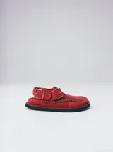 Slipper tipo guillermina confeccionada en gamuza color marrón, con plataforma de goma negra y doble hebilla ajustable. Presenta un pespunte decorativo en el borde inferior y cuenta con interior recubierto en cuero.