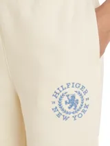 Pantalón de jogging color crema, con cintura elástica y cordón ajustable. Presenta un logo circular con el monograma TH bordado en azul en el muslo.