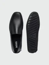 Mocasines de cuero negro con diseño clásico, costuras visibles en la puntera y detalle de logo grabado en el lateral.