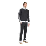 Campera deportiva Adidas modelo Beckenbauer, de color negro con detalles en blanco. Presenta cuello alto, cierre frontal completo, bolsillos laterales con cierre y las icónicas tres tiras de la marca en las mangas. El diseño incluye puños y cintura en tejido acanalado blanco y el logo del trébol bordado en el pecho.