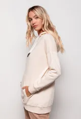 Canguro oversize color beige, de tela deportiva, con capucha ajustable con cordones y bolsillo tipo canguro en el frente.