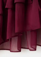 Blusa bordó de tejido fluido y semi transparente, con escote en V pronunciado, mangas largas abullonadas con volantes en los puños y detalles de volantes en el cuello y el ruedo.