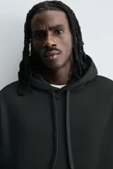 Sudadera tipo hoodie de corte relajado, confeccionada en tejido de algodón con interior cepillado. Presenta capucha con cordones ajustables, bolsillo frontal tipo canguro y terminaciones en rib en puños y ruedo.