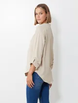 Blusa de gasa color beige, marca Floral & Ivy, con cuello a la base y escote en V. Las mangas son largas y regulables con presilla y botón.