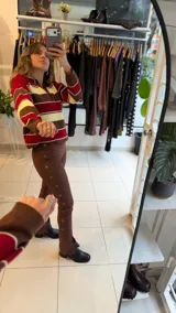 Sweater tejido de punto con diseño a rayas horizontales en tonos amarillo, celeste y marrón. Presenta un cuello polo con escote en V, mangas largas y un corte holgado.