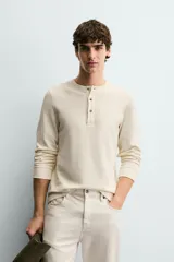 Camiseta de manga larga en tejido de estructura canalé, con cuello redondo y cierre frontal de botonadura. Presenta un corte relajado y puños acanalados.