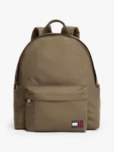 Mochila de diseño redondeado en color marrón, confeccionada en poliéster texturizado. Cuenta con un compartimento principal con cierre, un bolsillo exterior con cremallera y un bolsillo interior de malla. Incluye asa superior y correas ajustables y acolchadas. Presenta un parche tejido con el logo de Tommy Jeans en la parte delantera.
