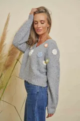 Buzo de punto color gris, con cuello en V, mangas largas y detalles de flores tejidas en varios colores en el frente.