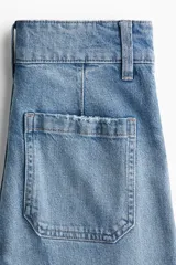 Jean de tiro alto con pierna amplia y corte holgado. Presenta cierre frontal con doble botón, bolsillos traseros de parche y pliegues marcados en el frente y la parte posterior.