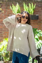 Sweater oversize de tejido de punto color beige, con cuello a la base y mangas largas acampanadas. Presenta detalles bordados a mano en color blanco en el frente, hombros y ruedo.