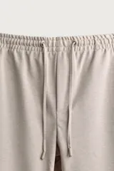 Pantalón jogger color beige de tejido transpirable y elástico con cintura elástica ajustable con cordón, bolsillos frontales y bajo con vuelta.