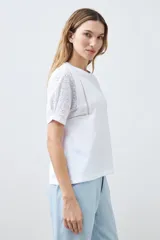 Remera blanca de algodón con mangas cortas de broderie, cuello redondo y corte recto.