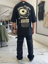 Remera oversize blanca de manga corta, con gran estampado en la espalda de una bandeja de vinilos y texto temático musical.
