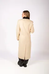 Tapado largo de paño color beige, con diseño de doble botonadura, solapas con detalle en contraste negro y bolsillos laterales con ribete negro.