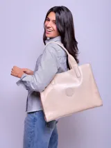 Cartera tipo tote de cuero color beige, con diseño minimalista, doble asa de hombro y logo circular grabado en el centro.