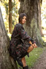 Vestido corto de lino con estampado floral en tonos tierra y verdes. Presenta cuello redondo, mangas largas amplias con puños terminados en volados y falda con volado en el ruedo. Incluye un lazo desmontable para ajustar la cintura.