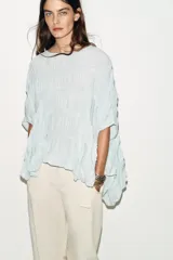 Top de cuello redondo color celeste con textura fruncida, mangas tipo capa y bajo asimétrico.