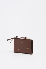 Billetera monedero de piel color marrón de Bimba y Lola, con estructura rígida y estampado de pequeñas palmeras doradas. Cuenta con cierre de cremallera superior con tirador de tela, logo impreso en el frente y tarjetero interior.