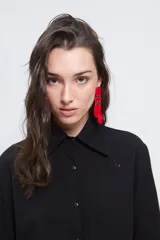 Camisa de corte holgado confeccionada en algodón tussor, con cuello clásico de tamaño ligeramente ampliado, mangas con pinzas laterales y puños anchos. Presenta cierre frontal con botones y un pequeño detalle bordado en el pecho.