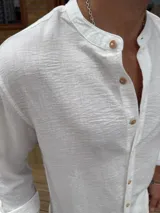 Camisa blanca de corte clásico con cuello mao, manga larga con puños abotonados y cierre frontal con botones de madera.