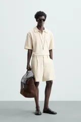 Bermuda de hombre color verde claro, de corte regular y tiro medio, con pinzas frontales, bolsillos laterales y bolsillos traseros de vivo. Cierre frontal con botón y cremallera.