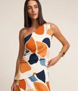 Blusa de hombro único confeccionada en crepé de poliéster, con diseño sin mangas, fruncidos laterales y bajo asimétrico. Presenta estampa abstracta en tonos blanco, naranja, azul marino, celeste y beige.