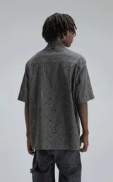 Camisa de manga corta con calce oversize, confeccionada en algodón con bordado tipo broderie y acabado con efecto desgastado. Presenta cuello clásico y cierre frontal con botones.