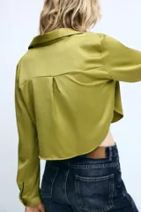 Camisa corta de acabado satinado, con cuello solapa, escote en pico y manga larga. Presenta cierre frontal con botones forrados a tono.