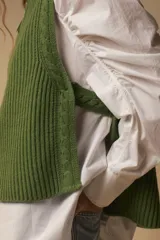 Chaleco tejido verde oliva con cuello alto, cierre metálico frontal y diseño de punto acanalado vertical.