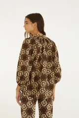 Blusa de corte relajado color marrón con estampado floral de margaritas, escote en V con cordones colgantes y mangas tres cuartos abullonadas con puños elastizados.