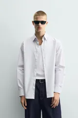 Camisa de corte regular fit confeccionada en tejido de algodón con diseño de rayas verticales finas. Presenta cuello italiano, manga larga con puños abotonados y cierre frontal mediante botonadura.