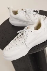 Zapatillas urbanas blancas de cuero con cordones moteados en blanco y negro y suela chunky.