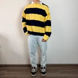 Buzo de manga larga con diseño a rayas horizontales amarillas y negras, corte boxy y cuello polo blanco con abertura en V.