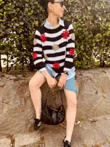 Sweater de punto con rayas horizontales blancas y negras, cuello redondo y flores bordadas en rojo y dorado. Corte clásico y mangas largas.