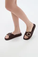 Sandalia plana de eco cuero negro, con tira ancha en el empeine decorada con una hebilla metálica dorada cuadrada y suela dentada.