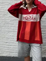 Sweater de punto rojo con rayas horizontales naranjas y blancas, cuello polo blanco y mangas largas. Presenta un diseño con letras curvas en el pecho.