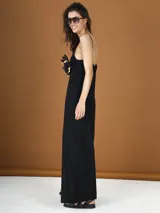 Mono largo negro de bretel fino con escote en V y detalle de flor en el pecho.