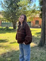 Buzo de tejido de punto en color marrón chocolate, con diseño oversize, cuello redondo y mangas largas abullonadas. Presenta detalles de líneas horizontales en color crudo y terminaciones en contraste en cuello, puños y ruedo.