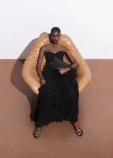 Vestido maxi largo negro de viscosa, palabra de honor y sin mangas. Presenta diseño evasé con detalle de volantes escalonados y cierre de cremallera lateral.