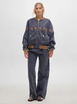 Pantalón jean de tiro alto y corte pinzado, con perneras de caída suelta y levemente anchas en el bajo. Posee pasador con hebilla en la parte trasera.