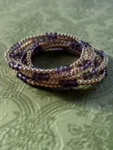 Pulsera elástica compuesta por una alternancia de cuentas metálicas doradas y cristales facetados de color violeta.
