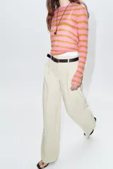 Pantalón recto color beige de tiro alto con pinzas delanteras, bolsillos frontales y falsos bolsillos de vivo en la espalda. Incluye un cinturón fino negro con hebilla dorada. Cierre frontal con cremallera, botón interior y gancho.